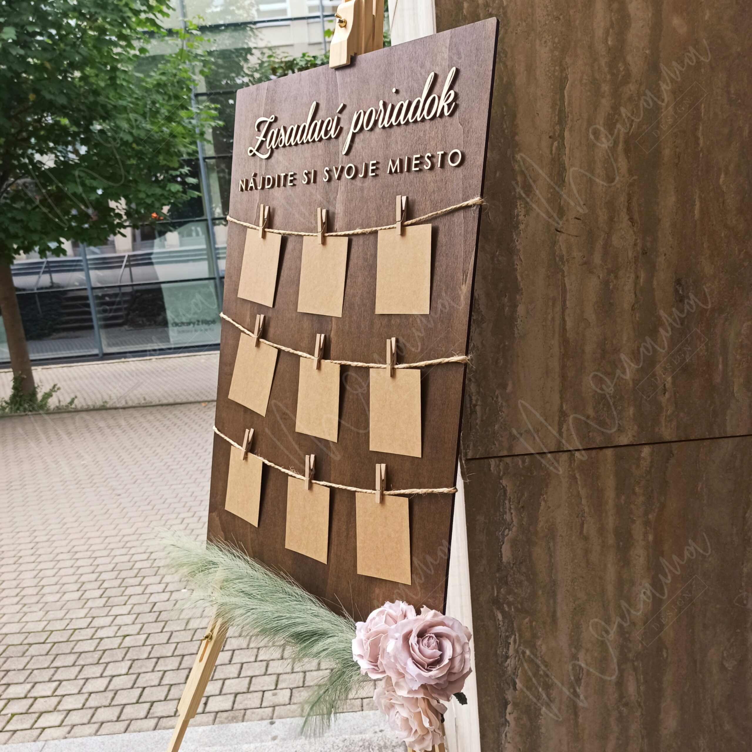 Rustikálny drevený zasadací poriadok so špagátom, drevenými kolíčkami a kraft kartičkami — seating chart na svadbu a event.