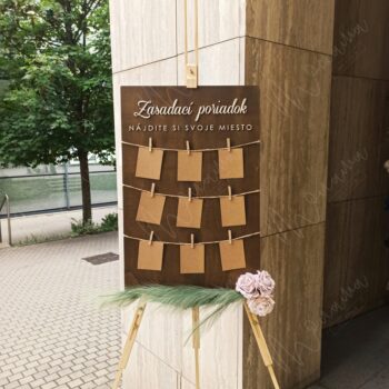 Rustikálny drevený zasadací poriadok so špagátom, drevenými kolíčkami a kraft kartičkami — seating chart na svadbu a event.