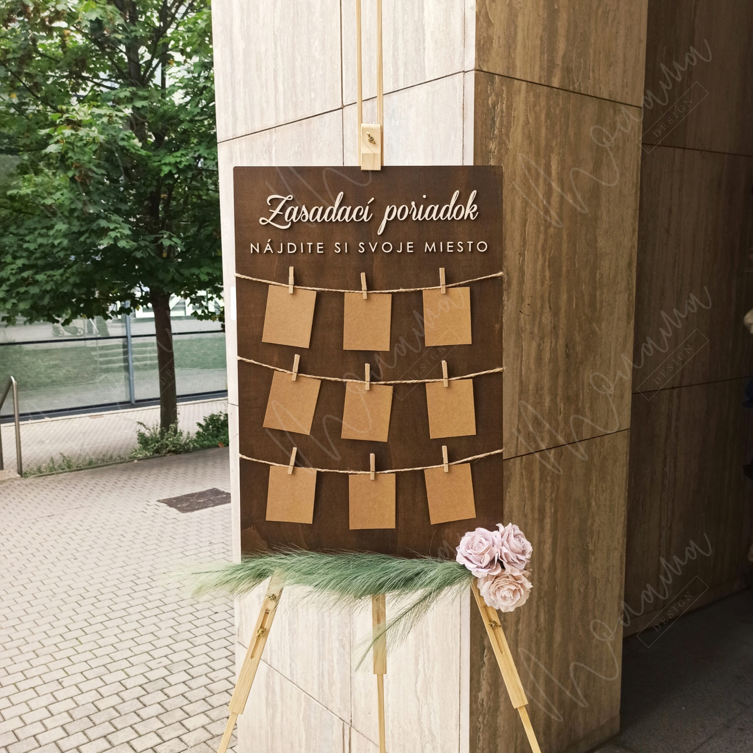 Rustikálny drevený zasadací poriadok so špagátom, drevenými kolíčkami a kraft kartičkami — seating chart na svadbu a event.