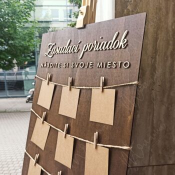 Rustikálny drevený zasadací poriadok so špagátom, drevenými kolíčkami a kraft kartičkami — seating chart na svadbu a event.