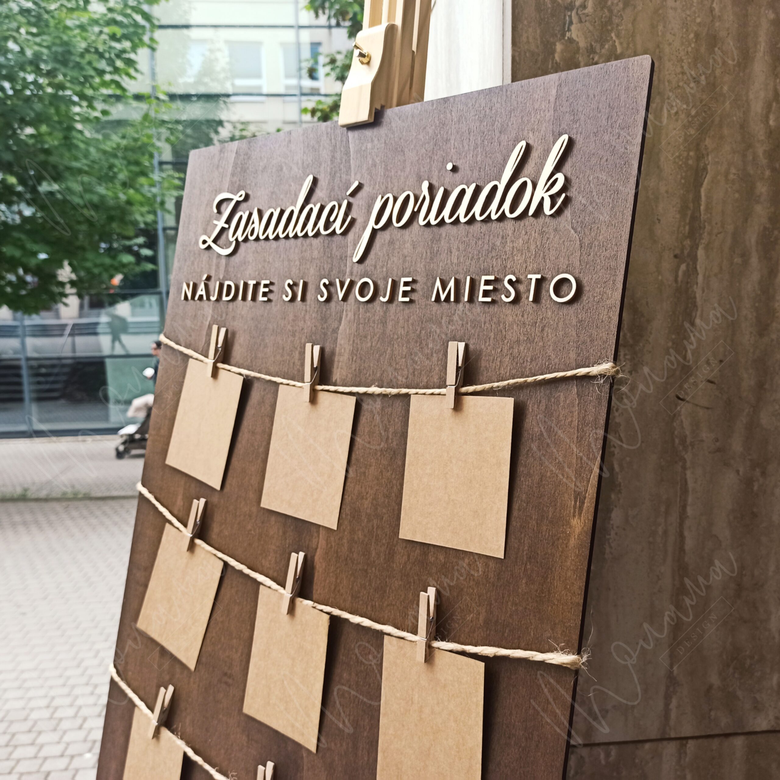 Rustikálny drevený zasadací poriadok so špagátom, drevenými kolíčkami a kraft kartičkami — seating chart na svadbu a event.