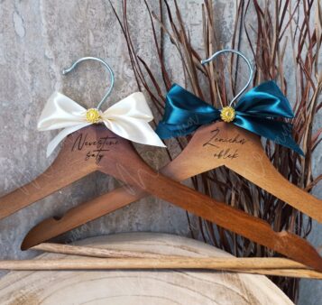 Svadobné vešiaky s nápisom ‚Nevestine šaty‘ a ‚Ženíchov oblek‘ – zdobené stuhami a kovovým háčikom, ideálne na fotenie svadobných detailov.
