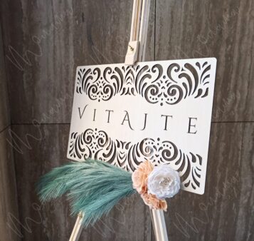 Drevená uvítacia tabuľa s gravírovaným nápisom ‚Vitajte na našej svadbe‘, zdobená kvetmi a pampovou trávou – elegantná svadobná výzdoba.