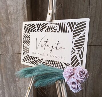 Uvítacia tabuľa na svadbu z dreva s nápisom ‚Vitajte na našej svadbe‘, ozdobená kvetmi a pampovou trávou – elegantný doplnok svadobnej výzdoby.