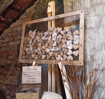 Svadobná uvítacia kniha hostí v drevenom ráme s priezračným plexisklom, naplnená drevenými srdiečkami, na ktorých môžu hostia zanechať odkaz.