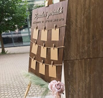 Rustikálny drevený zasadací poriadok so špagátom, drevenými kolíčkami a kraft kartičkami — seating chart na svadbu a event.